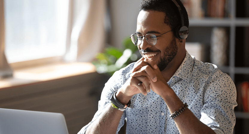 Student wearing glasses and an audio headset looking at their laptop and smiling.